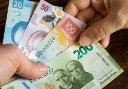 Dos manos intercambian billetes de 200, 100, 50 y 20 pesos mexicanos con un fondo color café. 