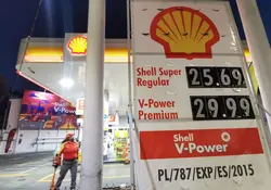 Estación de gasolina Shell con letrero de precios y un trabajador. 