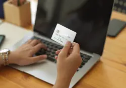 Persona sostiene una tarjeta de crédito frente a una computadora.