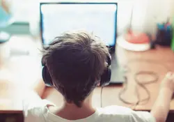 Niño con audífonos puestos navegando por internet a través de una computadora 