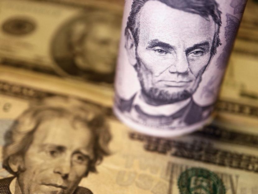 Dos billetes dólar acostados y uno enrollado con la cara de Lincoln.