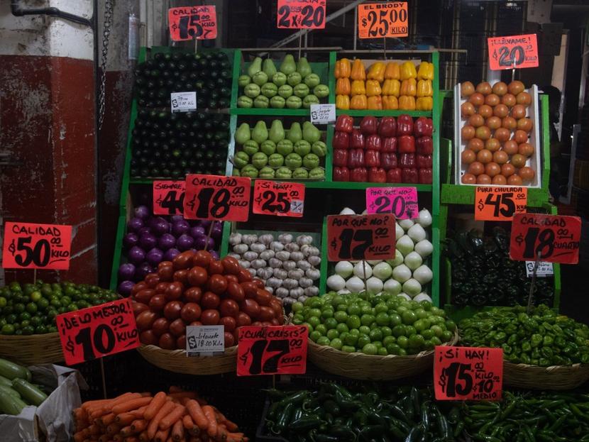 Un puesto de verduras con letreros que muestran los precios de venta en un mercado. 