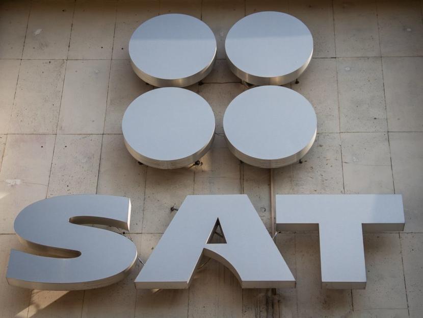 Logotipo del SAT en color plateado sobre una pared. 