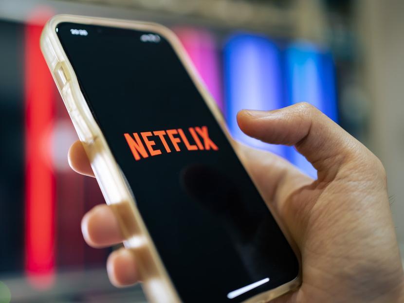 Una mano sostiene un celular que muestra el ícono de Netflix en la pantalla. 