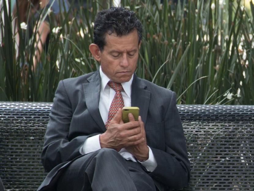 Hombre sentado en banca usando celular
