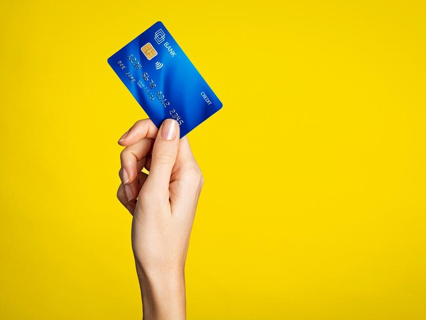 La mano de una mujer sostiene una tarjeta de crédito azul y un fondo de color amarillo. 