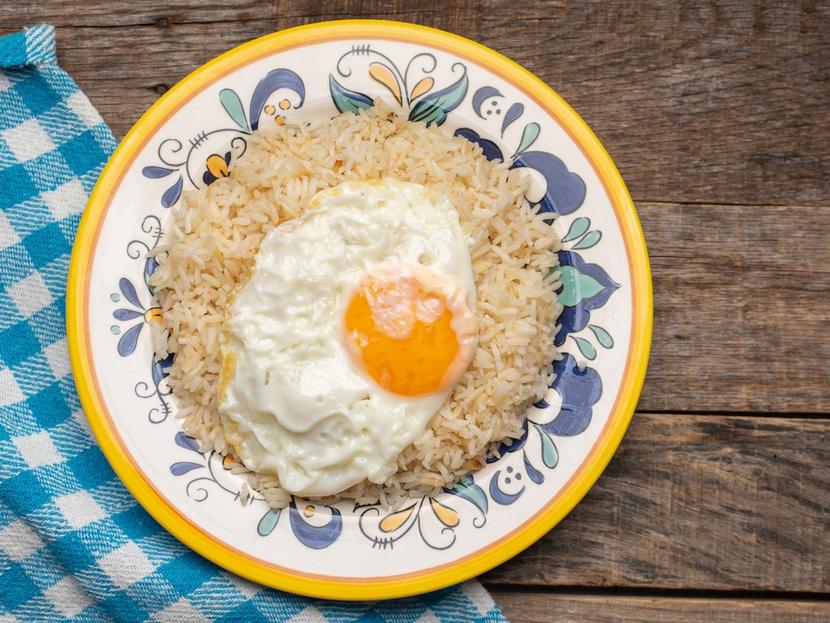 Un plato floreado con comida de arroz y un huevo colocado sobre una mesa de madera. 
