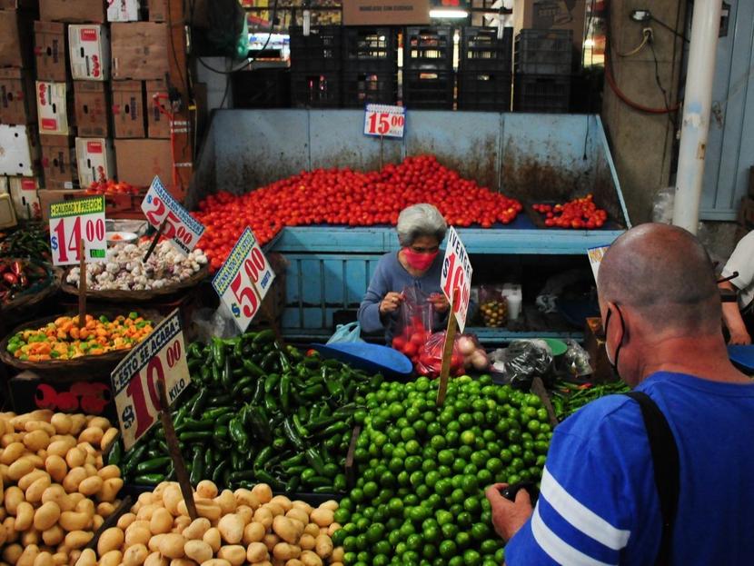 Un hombre compra verduras en un puesto de mercado popular y una señora adulta lo atiende. 