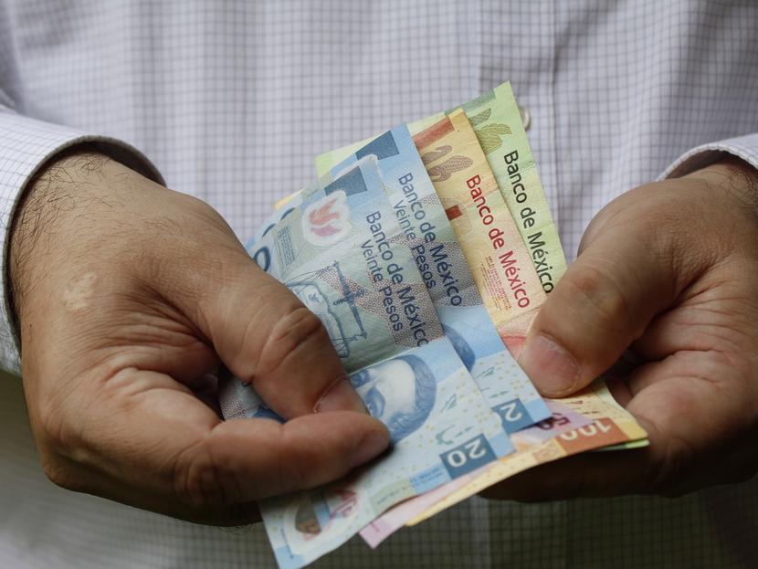 Las manos de una persona sostienen billetes de 20, 50, 100 y 200 pesos mexicanos. 