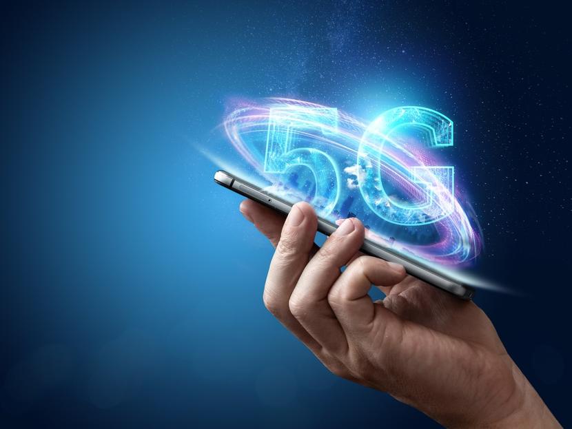 Una mano sostiene un celular con el símbolo de 5G flotando. 
