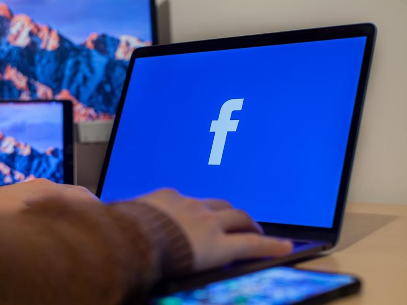 computadora sobre escritorio con fondo de pantalla azul y logo de facebook 