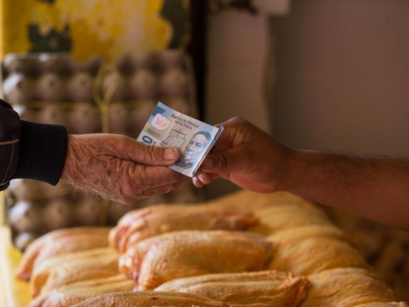 Una mano paga con un billete de 20 pesos y otra lo recibe en un negocio de venta de pollos. 