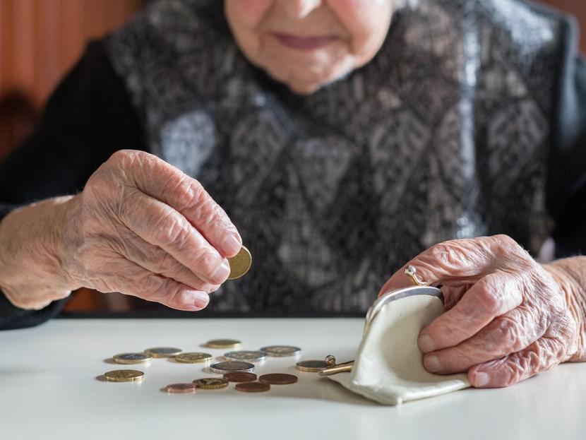 Una mujer adulta cuenta sus monedas sobre una mesa y sostiene su monedero. 