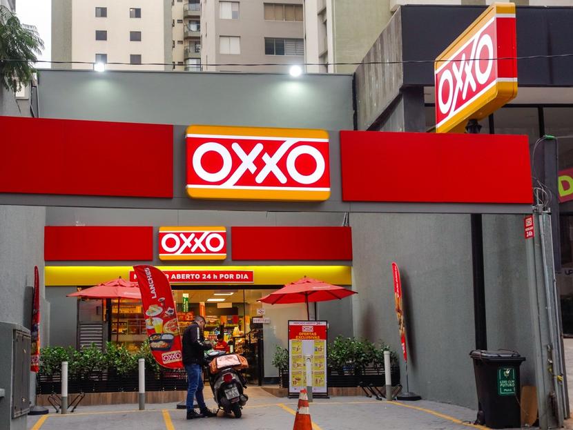 Entrada de tienda comercial Oxxo con una persona parada al lado de su moto.  