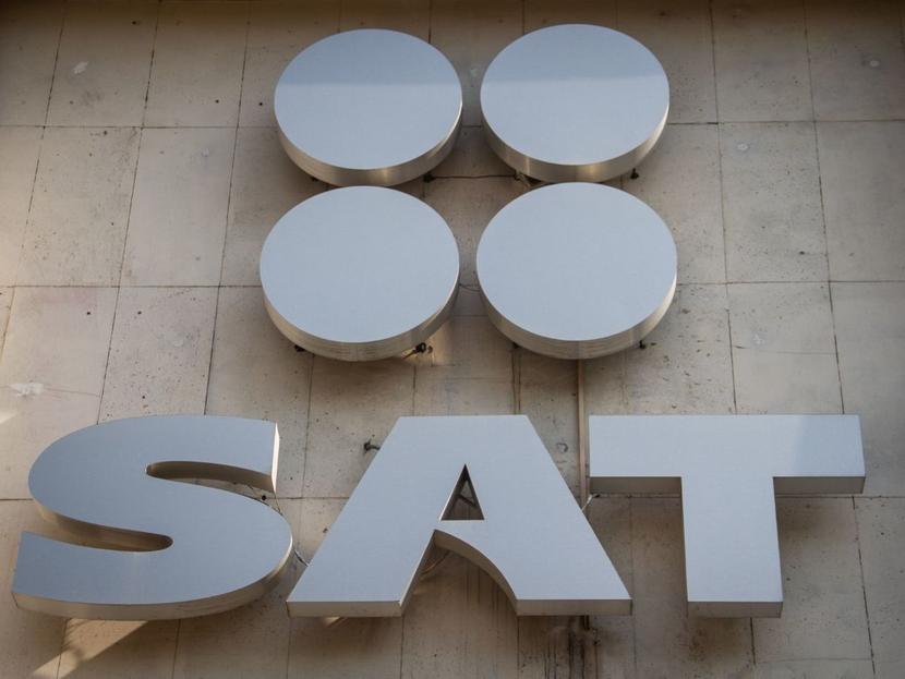 Logotipo del SAT en color plateado y sobre una pared. 