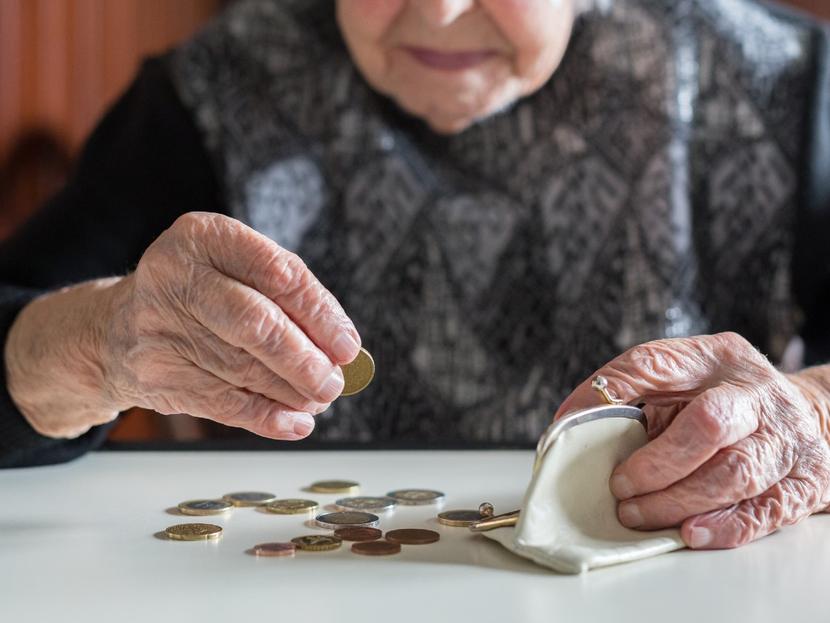 Las manos de una persona adulta mayor acomodan monedas en una cartera. 