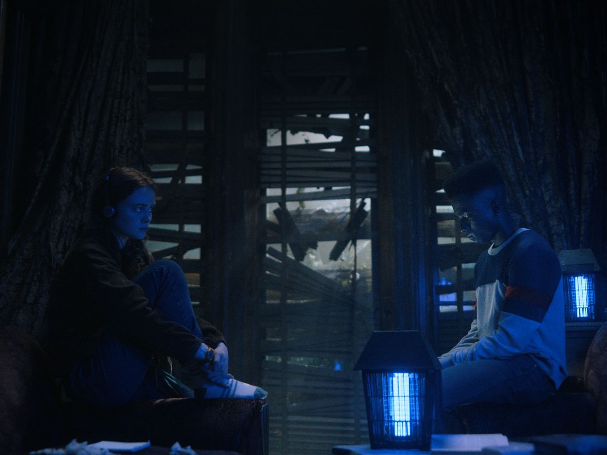 Max y Lucas Stranger Things sentados frente luz color azul