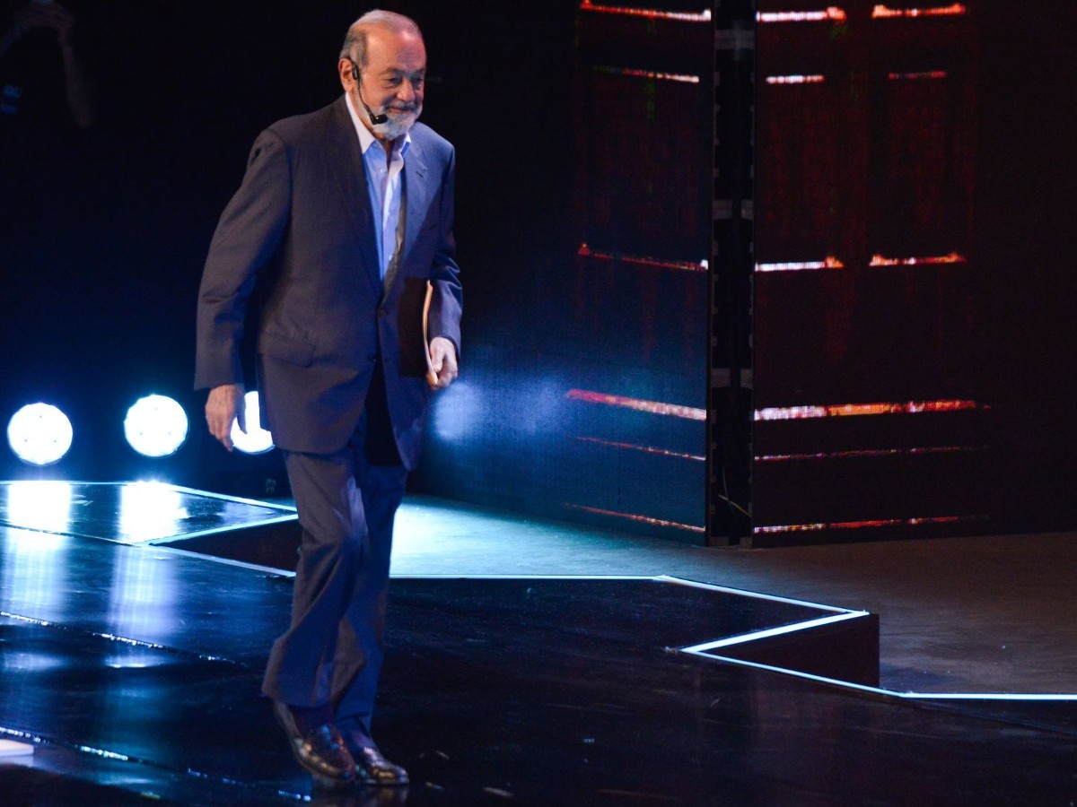 El empresario Carlos Slim caminando sobre un escenario y con una diadema de micrófono. 