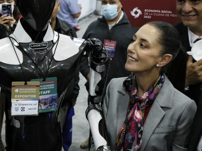 Claudia Sheinbaum, Jefa de Gobierno de la Ciudad de México, sonriendo al observar el prototipo de un robot en una exposición. 