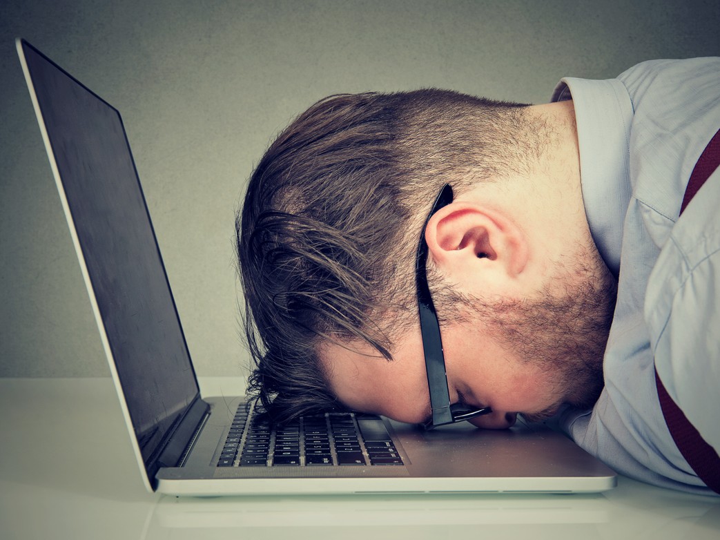 Un hombre acostado sobre el teclado de una laptop simulando estrés. 