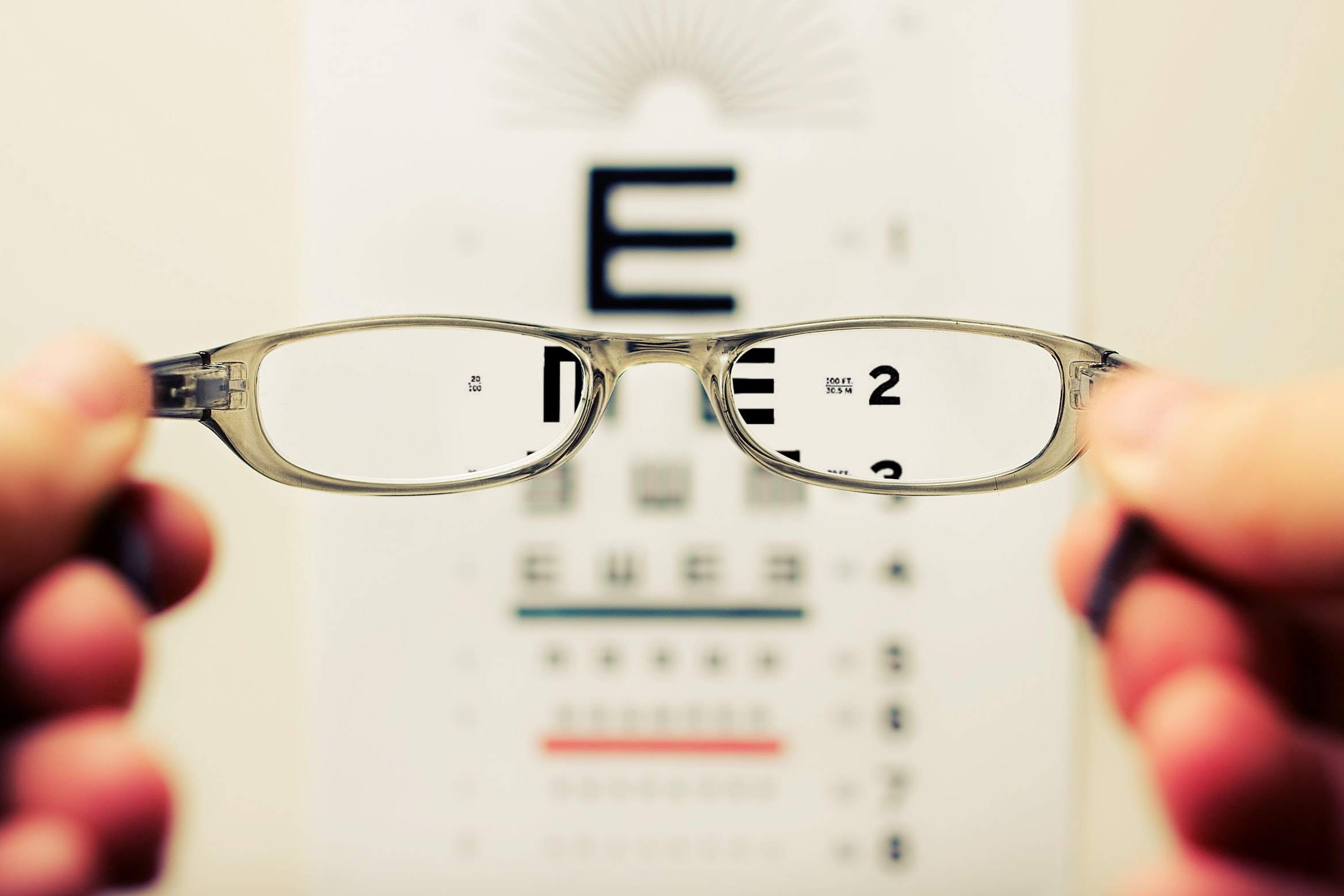 Manos sosteniendo lentes sobre fondo de letras para examen visual. 