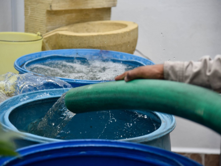 Mano sostiene una manguera depositando agua potable en botes de plástico. 