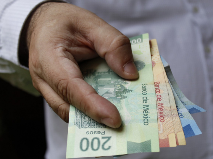 Una mano sostiene billetes de 200, 100 y 20 pesos mexicanos. 