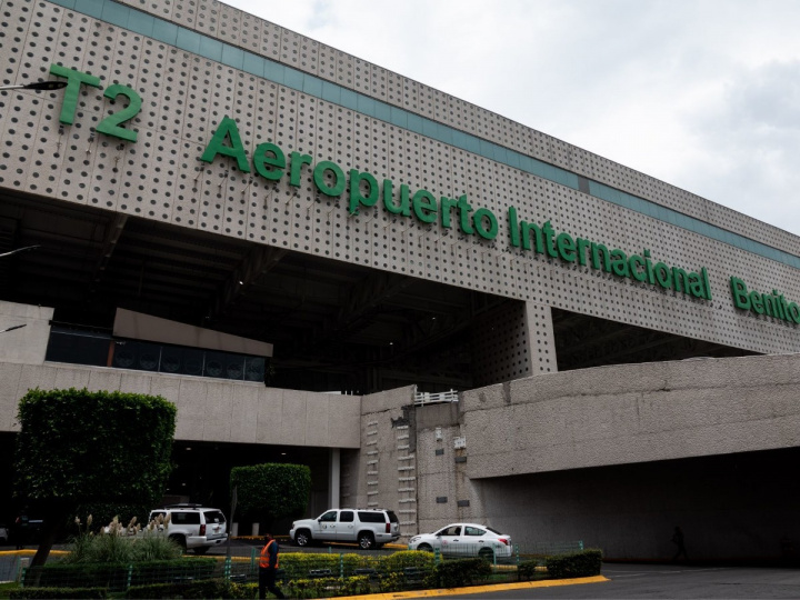 La fachada de la Terminal 2 del Aeropuerto Internacional de la ciudad de México (AICM) con autos blancos y un pequeño jardín. 