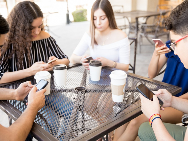 Varios jóvenes de la generación Z sentados en una mesa y utilizando su celular. 