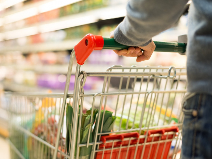 Una persona empuja un carrito del supermercado con varios productos. 