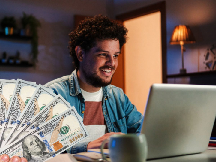 Hombre frente a computadora junto a dólares para ilustrar ¿Dónde te pagan por escribir? Gana en dólares y hazlo desde donde sea