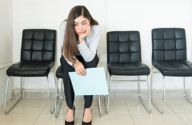 Una mujer sentada en una sala de espera y sostiene un folder. 