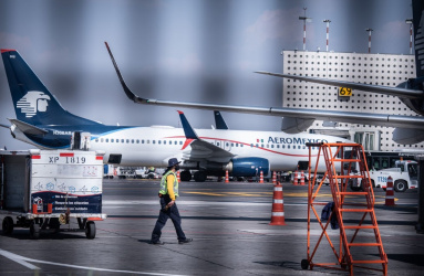 Aviones de Aeroméxico estacionados en el aeropuerto y un trabajador marinado en la pista de aterrizaje. 