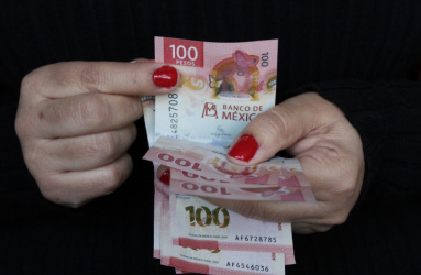 Las manos de una mujer con uñas pintadas maneja billetes de 100 pesos mexicanos. 