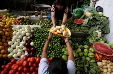 Dos señoras en un mercado intercambiando verduras sobre puesto de verduras
