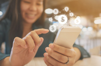 Mujer sentada en una mesa, sosteniendo celular en manos con iconos de dinero emergiendo 