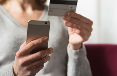 Mujer sentada sosteniendo un celular en una mano y una tarjeta en la otra 