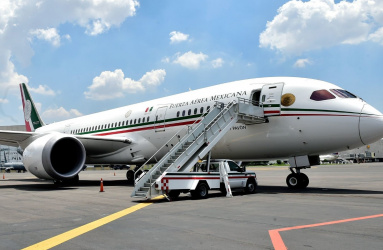 Avión presidencial estacionado en una pista aérea con escaleras y una camioneta estacionada. 