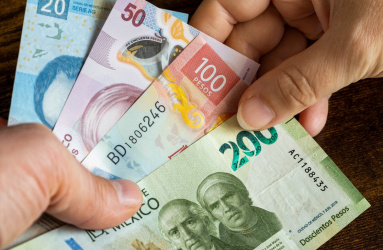 Dos manos intercambian billetes de 100, 200, 20 y 50 pesos mexicanos. 