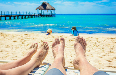 Los pies de dos personas llenos de arena frente a la orilla del mar. 