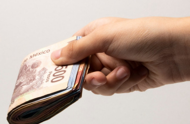 Una mano sostiene un fajo de billetes de pesos mexicanos. 