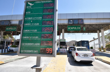 Caseta de autopista en México con letrero de tarifas y autos formados. 