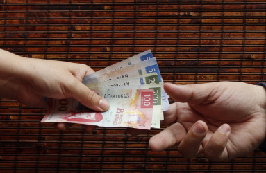 Dos manos intercambian billetes de 100, 200 y 500 pesos mexicanos con un fondo color café. 