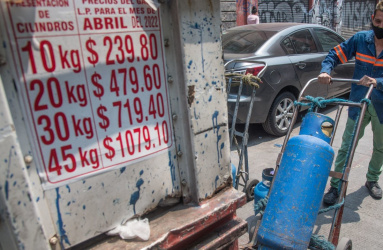 Un camión repartidor de gas LP con el letrero de los precios y una persona empujando un tanque. 