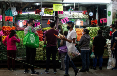Varias personas esperando ser atendidas en un local de verduras ubicado en un mercado popular. 