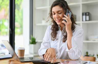 Una mujer sentada en un escritorio hablando con un teléfono celular en la mano. 
