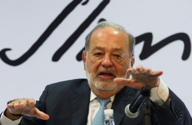El empresario Carlos Slim hablando frente a un micrófono y expresándose con las manos. 